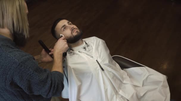 Парикмахер бреет бороду клиента в парикмахерской — стоковое видео