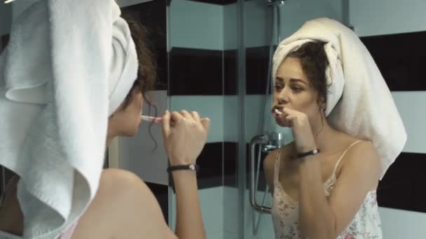 Menina bonita escovando os dentes no banheiro com uma toalha na cabeça. O reflexo no espelho. O conceito de autocuidado, procedimentos de banho — Vídeo de Stock