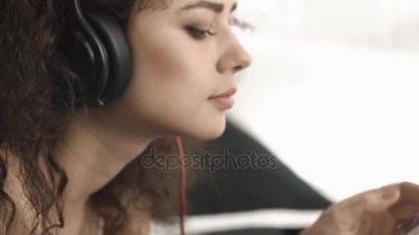 Genç kadın onun yatak odasında telefon kulaklık ile müzik dinlemek. En sevdiği şarkı için smartphone üzerinde dans kıvırcık saçlı kız, o iyi bir ruh hali vardır. Yakın çekim