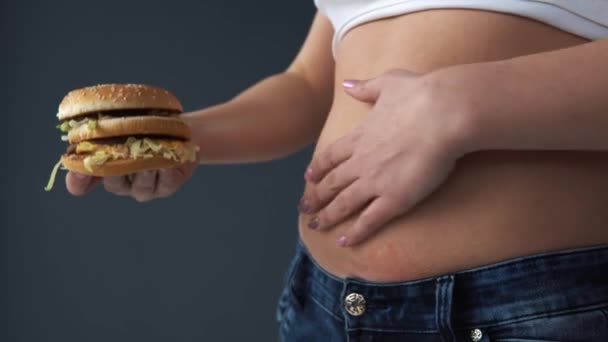 Túlsúlyos nő intézkedés kerülete a hasára, hamburger ellen. Gyorsétterem, túlevés, a mérgezés fogalma — Stock videók