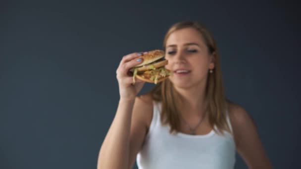 Obézní žena s hamburger na šedém pozadí. Ona si myslí, nebo jíst fast food — Stock video