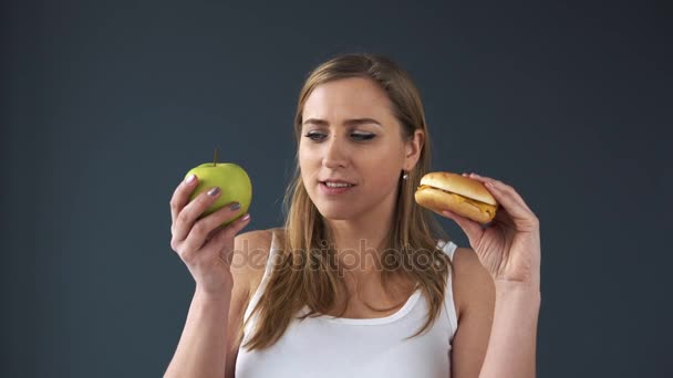 Túlsúlyos nő nem tudok választani mit eszik, az apple vagy a burger. Ő úgy dönt, hogy az alma. A koncepció az egészséges táplálkozás — Stock videók