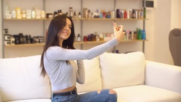 Krásná mladá dívka fotografování na sebe v make-up Studio. Ona sedí na gauči — Stock video