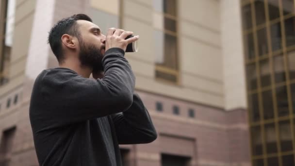 Mladý muž šťastný vousy mluví o smartphone a pití kávy na ulici při západu slunce — Stock video