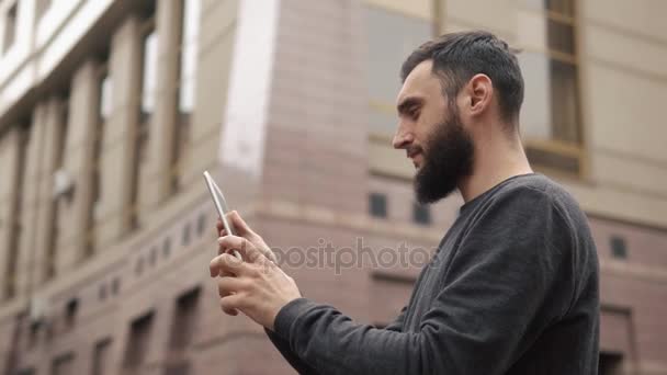 Mladý muž šťastný vousy pomocí tabletového počítače na ulici při západu slunce — Stock video