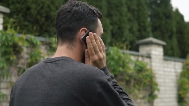 Young man with beard talking on the phone near his country house, motion camera — Stock Video