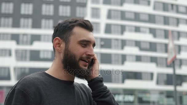 高層ビルの近くに電話で話しているひげを持つ若者 — ストック動画