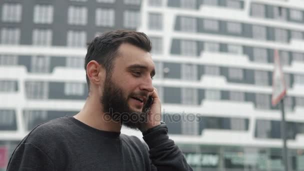 Joven con barba hablando por teléfono cerca de rascacielos — Vídeos de Stock