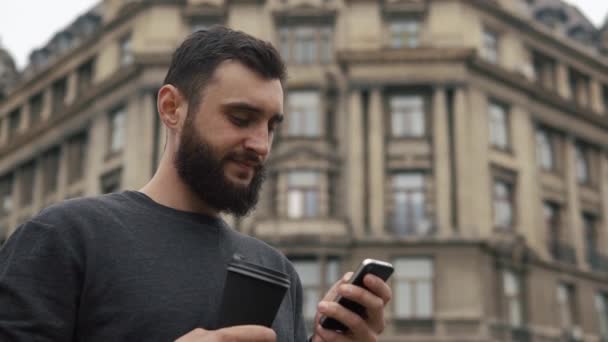 Чоловік перевіряє свій смартфон і п'є каву — стокове відео