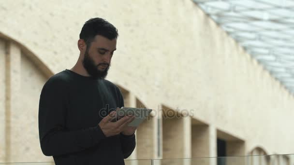 El hombre comprueba su tableta de pie en la sala brillante — Vídeo de stock