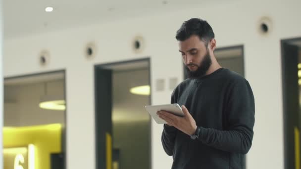 L'uomo controlla il suo tablet in piedi nella luminosa sala — Video Stock