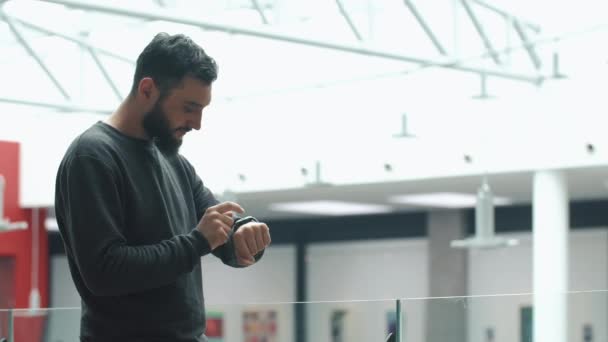 Homem verifica seu relógio inteligente em pé no salão brilhante — Vídeo de Stock