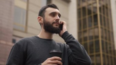 Smartphone üzerinde konuşmak ve içme kahve sokakta günbatımında mutlu sakal genç adam