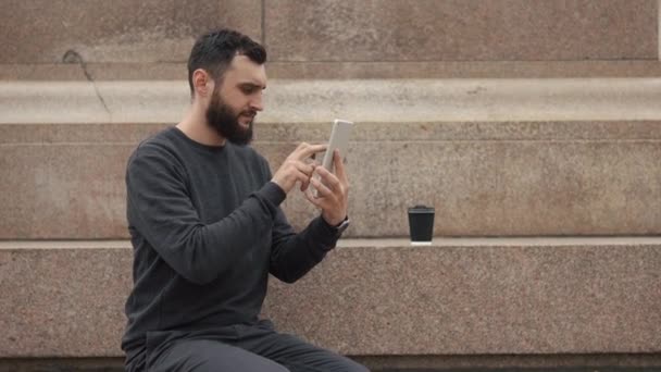 El hombre trabaja en la tableta sentado en los pasos — Vídeos de Stock