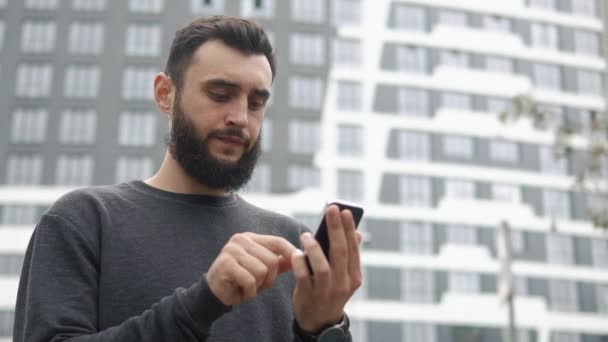 Homem digita algo em seu smartphone — Vídeo de Stock