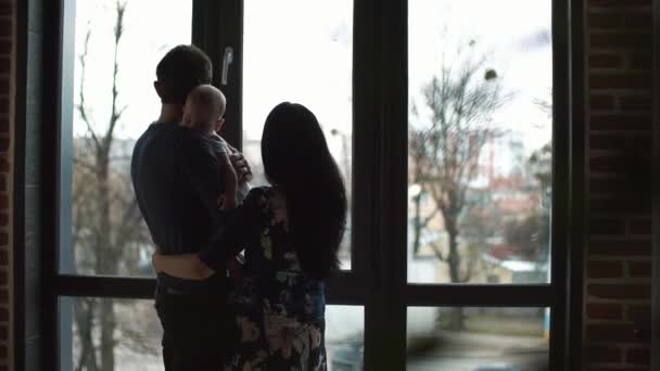 Famille rêveuse se tient avec un enfant devant la fenêtre panoramique — Video