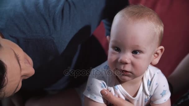 Родители держат маленького голубоглазого мальчика на руках, сидя на полу. — стоковое видео