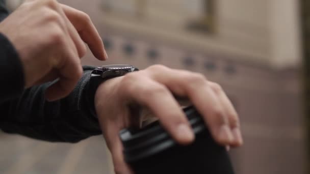 Vousatý muž kontroluje své chytré hodinky postavení s šálkem kávy — Stock video