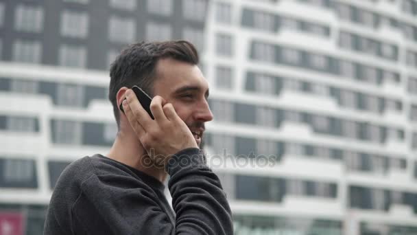 Мужчина говорит по своему смартфону, гуляя по городу — стоковое видео