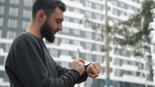 Bearded man checks his smart watch standing somewhere in the city — Stock Video