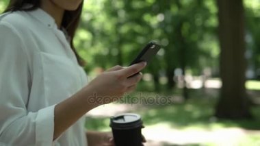 Kadın parkta kahve ile onun telefon ayakta denetler