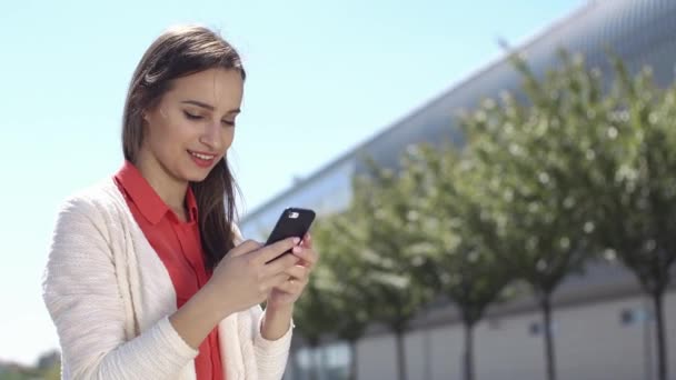 Жінка друкує щось у своєму телефоні, сидячи зовні — стокове відео