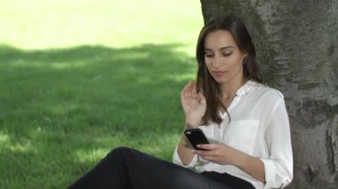 İş kadını Park ağacın altında oturup telefonunu denetler