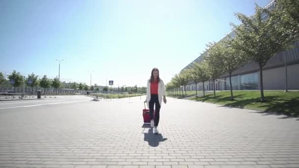 Pretty woman in red shirt walks with suitcase outside in a sunny day — Stock Video