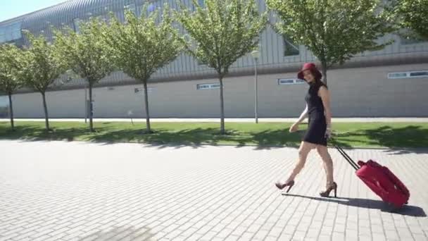 Frau mit rotem Hut geht mit rotem Koffer nach draußen — Stockvideo