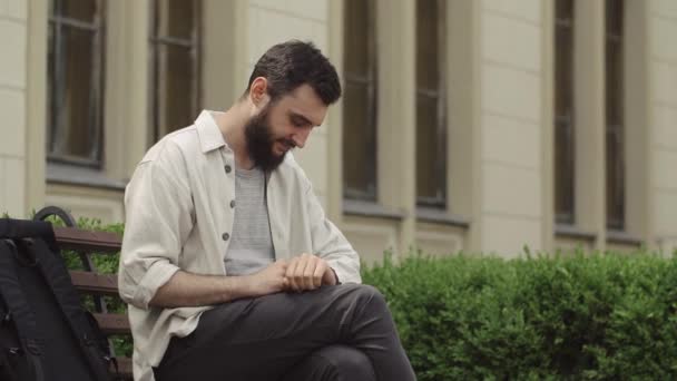 Man arbetar med sin smartwatch som sitter på bänken — Stockvideo