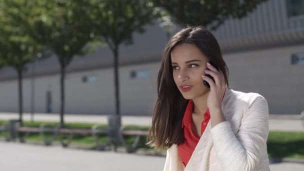 Женщина разговаривает по телефону, сидя снаружи — стоковое видео