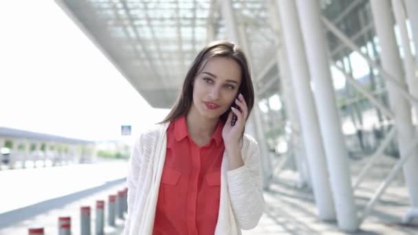 Mulher de camisa vermelha fala ao telefone andando com uma mala — Vídeo de Stock