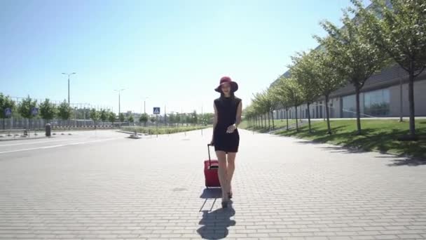 Γυναίκα με το κόκκινο καπέλο περπατάει με κόκκινη βαλίτσα έξω από — Αρχείο Βίντεο