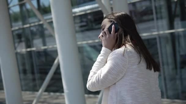 Vrouw in rood shirt gesprekken over de telefoon lopen met een koffer — Stockvideo