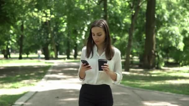 Женщина пьет кофе и проверяет телефон в парке. — стоковое видео
