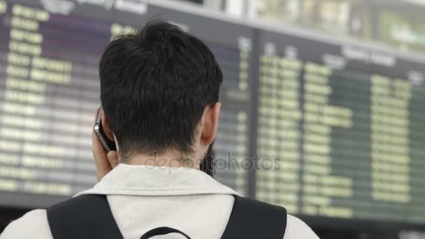 Бородач разговаривает по телефону, стоя в аэропорту — стоковое видео