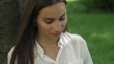 İş kadını Park ağacın altında oturup telefonunu denetler