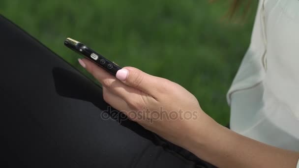 ビジネスの女性が公園の木の下で座っている彼女の携帯電話をチェックします。 — ストック動画