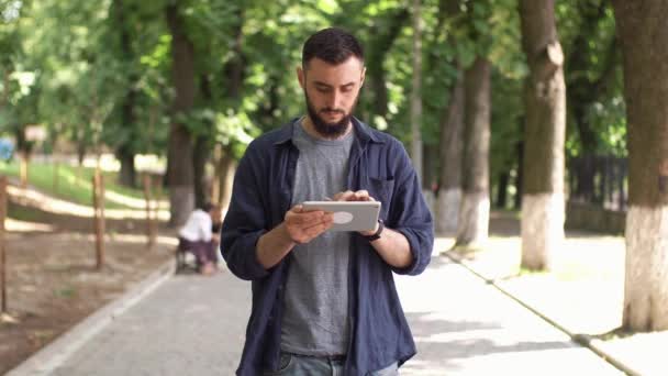 El hombre trabaja con la tableta de pie en el parque — Vídeos de Stock