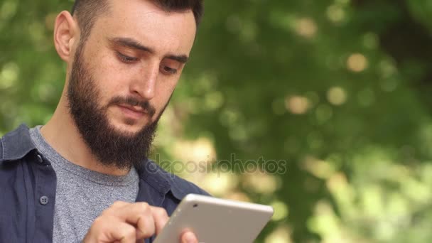 El hombre trabaja con la tableta de pie en el parque — Vídeo de stock