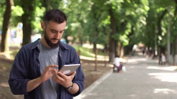 Człowiek działa z tabletu stojący w parku — Wideo stockowe