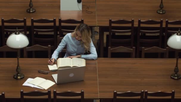 Estudiante trabaja con libros y laptop en la biblioteca — Vídeos de Stock