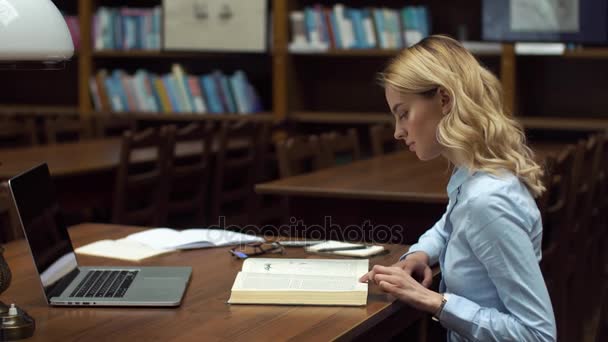 Σπουδαστής δουλεύει με βιβλία και φορητό υπολογιστή στη βιβλιοθήκη — Αρχείο Βίντεο