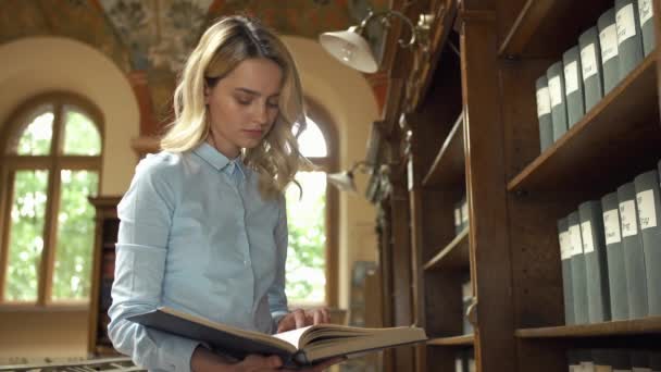 Студент читает книгу, стоящую в библиотеке — стоковое видео