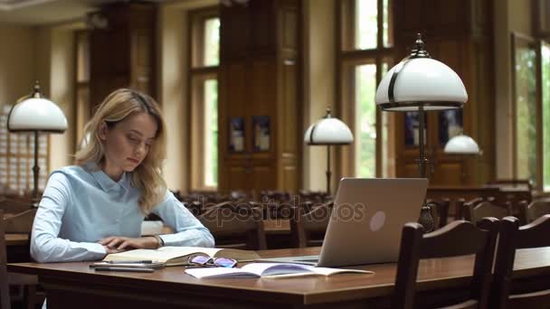 Estudante trabalha com livros e laptop na biblioteca — Vídeo de Stock