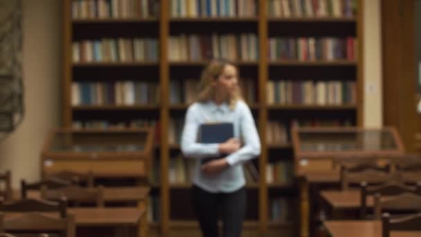 Estudiante camina con gran libro en la biblioteca — Vídeo de stock