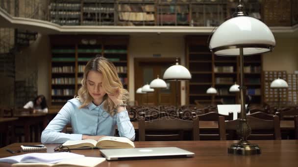 Estudante trabalha com livros e laptop na biblioteca — Vídeo de Stock