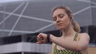 Kadın fitness elbiseli bankta oturan ve fitness bileziğini kontrol müzik dinliyor