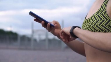 Kadın fitness elbiseli telefon ve fitness bileziğini denetler