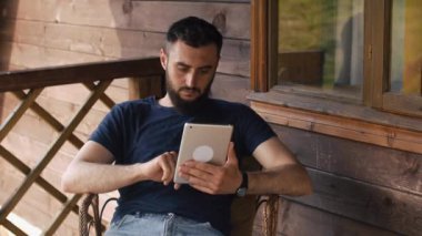 bir ülkenin ev verandada otururken tablet genç sakallı biri kullanır